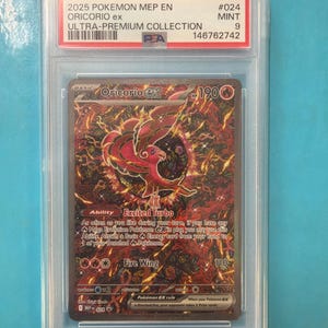 May include: A graded Pokémon card featuring Oricorio ex from the Ultra-Premium Collection. The card is encased in a protective case and has a red and gold design with the text "Fire Wing" and "Excited Turbo". The card is graded as Mint 9.