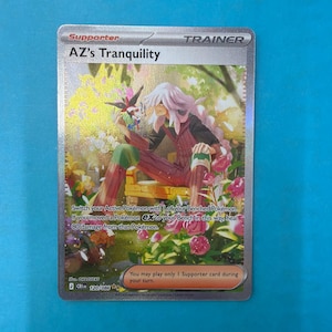 Può includere: Una carta collezionabile Pokemon con bordo argentato intitolata AZ's Tranquility, che raffigura un personaggio dai lunghi capelli bianchi seduto su una panchina gialla in un giardino. La carta include testo sulle regole, una creatura e fiori.
