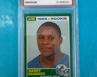 Può includere: Una carta rookie di football di Barry Sanders del 1989, valutata NM-MT 8 da PSA, in un contenitore protettivo trasparente. La carta presenta Barry Sanders e il testo "RUNNING BACK". La carta ha un design verde e bianco.