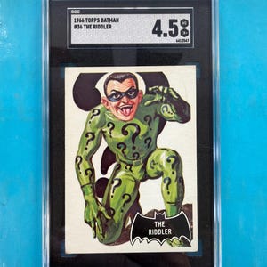 Könnte beinhalten: Eine 1966 Topps Batman Sammelkarte, Nummer 36, mit dem Riddler. Die Karte ist in einem schwarzen SGC-Gehäuse mit der Bewertung 4.5 eingeschlossen. Die Illustration zeigt eine grün gekleidete Figur mit Fragezeichen, Maske und Fledermaus-Etikett.