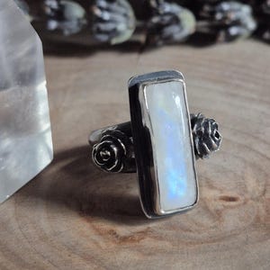 Puede incluir: Un anillo de plata con una piedra de luna rectangular y dos acentos de rosas de plata.