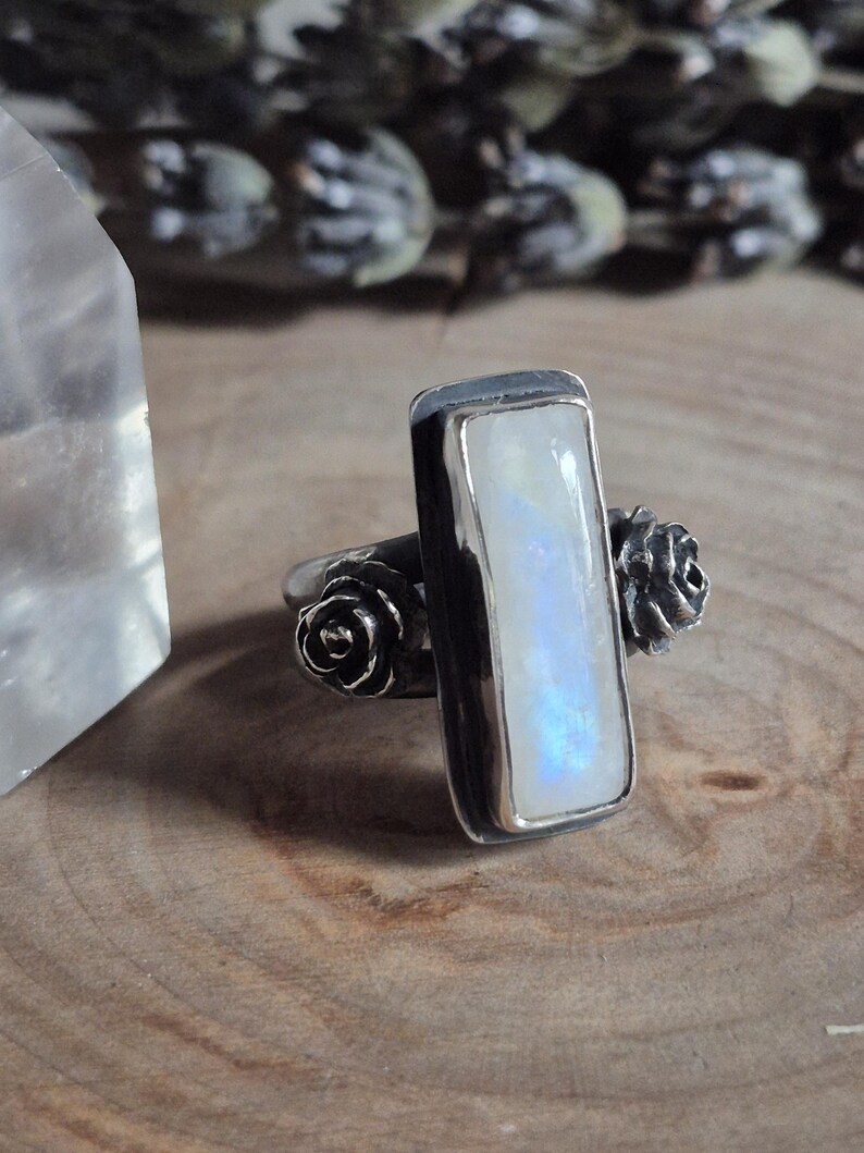 Puede incluir: Un anillo de plata con una piedra de luna rectangular y dos acentos de rosas de plata.