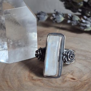 Puede incluir: Un anillo de plata con una piedra de luna rectangular y dos acentos de rosas de plata.