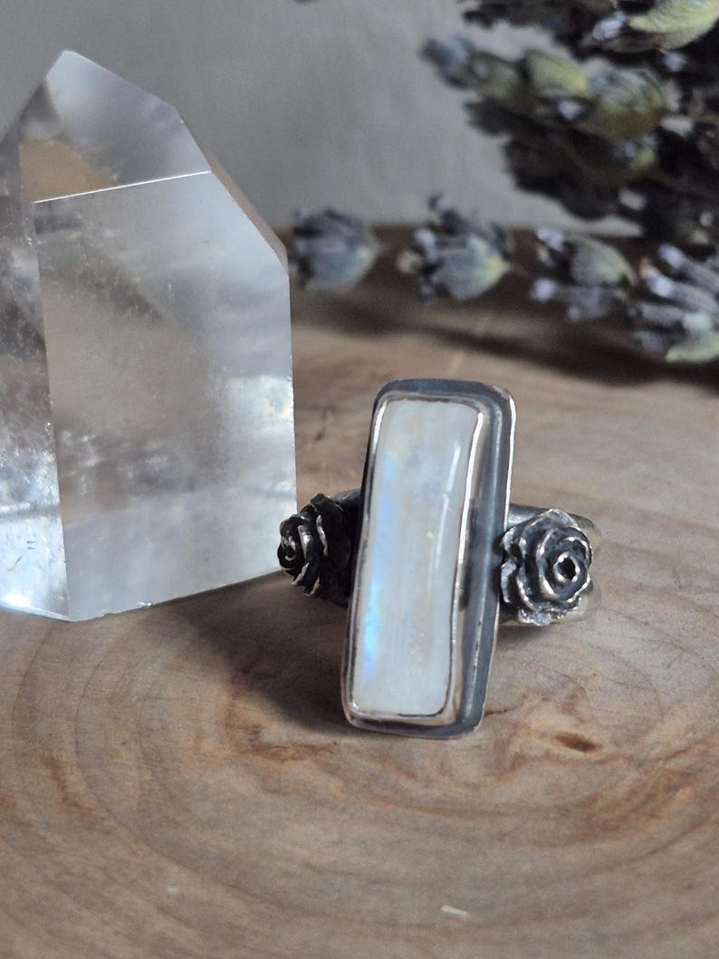 Puede incluir: Un anillo de plata con una piedra de luna rectangular y dos acentos de rosas de plata.