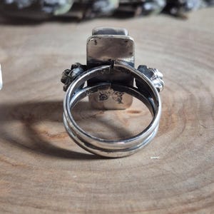 Puede incluir: Un anillo de plata con una piedra rectangular engastada en el centro. El anillo est&aacute; dise&ntilde;ado con dos bandas que se envuelven alrededor del dedo y se unen en la parte superior de la piedra.