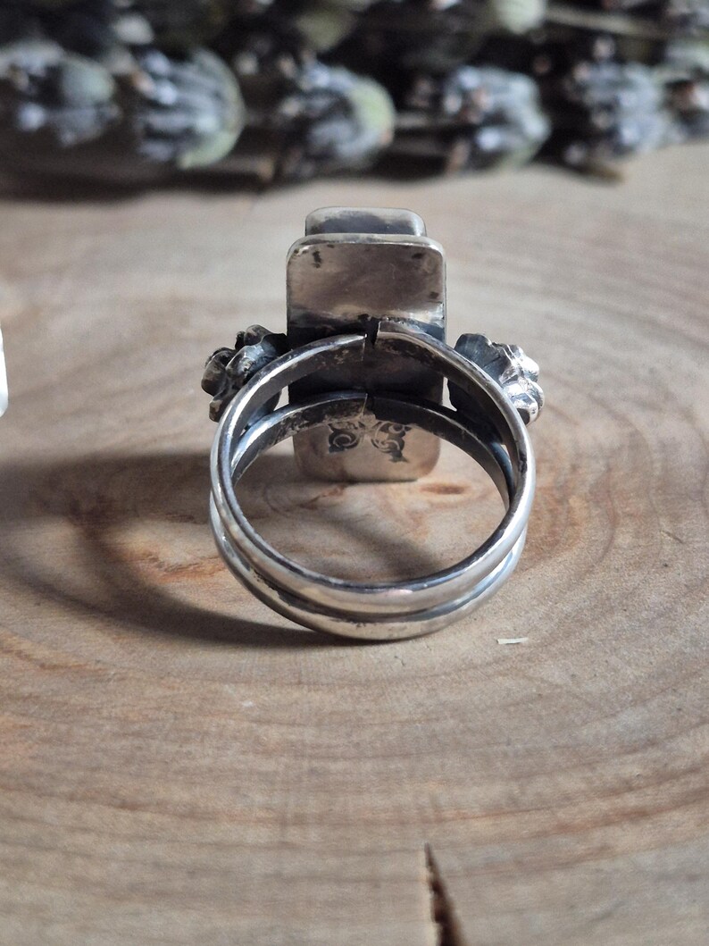 Puede incluir: Un anillo de plata con una piedra rectangular engastada en el centro. El anillo est&aacute; dise&ntilde;ado con dos bandas que se envuelven alrededor del dedo y se unen en la parte superior de la piedra.