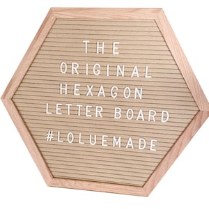 May include: Hexagon-shaped letter board with a light brown, textured surface and a light wood frame. The text "THE ORIGINAL HEXAGON LETTER BOARD" is displayed in white letters. The hashtag "#LOLUEMADE" is also visible.