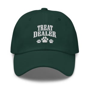 May include: A dark green baseball cap with the embroidered text "TREAT DEALER" above three paw prints. The hat has a curved brim and a fabric strap with a metal buckle on the back for adjustment. This cap is a fun accessory for dog lovers.