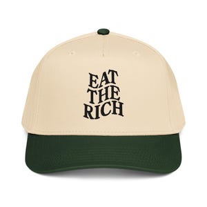 Könnte beinhalten: Baseballkappe mit cremefarbener Krone und dunkelgrünem Schirm. Auf der Vorderseite der Kappe steht in schwarzer Schrift "EAT THE RICH" in einer stilisierten Schriftart. Die Kappe hat einen dunkelgrünen Knopf oben.