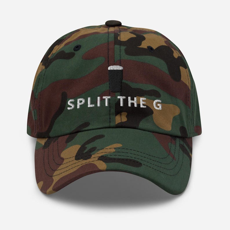 Puede incluir: Gorra de b&eacute;isbol de camuflaje con la inscripci&oacute;n "SPLIT THE G" bordada en blanco. La gorra tiene un bot&oacute;n negro y una visera curvada. El patr&oacute;n de camuflaje incluye tonos verdes, marrones y beige.
