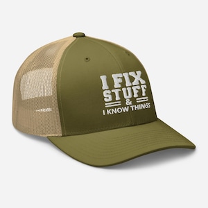 Puede incluir: Gorra de camionero verde oliva con la parte trasera de malla beige. La parte delantera muestra el texto blanco "I FIX STUFF & I KNOW THINGS". La gorra tiene una visera curva y un botón en la parte superior.