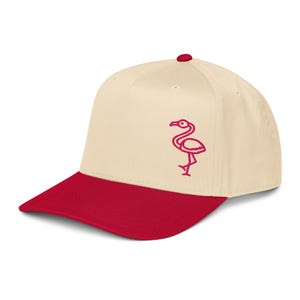 May include: A baseball cap with a cream-colored crown and a red brim. A red flamingo logo is embroidered on the front. The cap has a curved brim and a button on top.