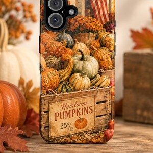 May include: A phone case featuring a rustic wooden crate filled with various heirloom pumpkins and gourds. A sign on the crate reads Heirloom PUMPKINS 25 cents/LB. The background shows a storefront with an American flag and autumn foliage.