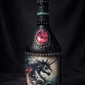 May include: Black decorative bottle with a unicorn illustration. The bottle has a crown-shaped stopper and is decorated with silver embellishments and a large pink gem. The unicorn has a flowing mane in shades of pink, white, and blue.