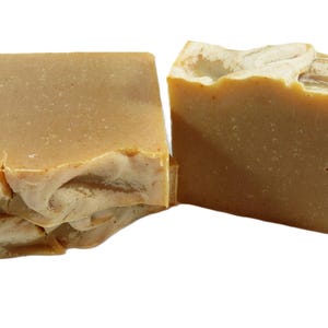 Op de afbeelding: Drie stukken handgemaakte zeep. De zeep is lichtbruin van kleur met een getextureerde, gebroken witte toplaag. De stukken zijn in rechthoekige vormen gesneden, met zichtbare natuurlijke variaties.