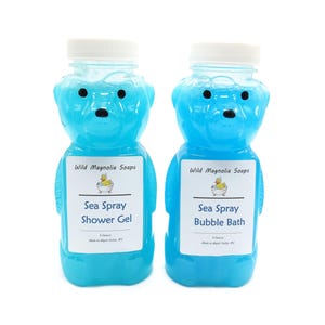 Puede incluir: Dos botellas con forma de oso de gel de ducha y baño de burbujas Sea Spray azules. Las botellas tienen tapas blancas y etiquetas con el texto "Wild Magnolia Soaps" y "Sea Spray". Cada botella contiene 237 ml.