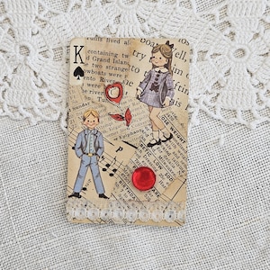 May include: A vintage-style card featuring illustrations of a boy and girl in old-fashioned clothing, along with a red heart and button. The card is decorated with lace and text from an old book, creating a nostalgic aesthetic.