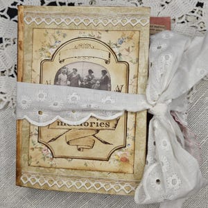 May include: A vintage-style journal with a floral design and the word "memories" on the cover. The journal is tied with a white eyelet ribbon. The cover features a sepia-toned photograph of a group of people.