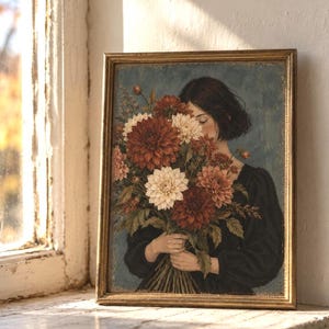Peut inclure: Une impression encadrée représentant une personne aux cheveux bruns vêtue d'un vêtement noir à manches longues, tenant un grand bouquet de dahlias rouge foncé et blancs sur un fond bleu sourd. Le cadre doré mesure 12,7 par 17,8 cm.