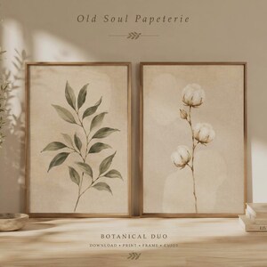 Peut inclure: Deux cadres muraux présentant des illustrations botaniques sur fond beige. L'impression de gauche montre une branche aux feuilles vertes, tandis que celle de droite représente une tige de coton. Texte : Old Soul Papeterie et Botanical Duo.