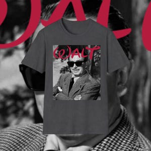 May include: A charcoal grey t-shirt with a black and white image of a man in sunglasses and a suit. The word "WALT" is printed in red above the image. The shirt has short sleeves and a crew neck.