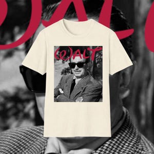 May include: A cream-coloured t-shirt with a black and white image of a man wearing sunglasses. The word "WALT" is printed in red cursive script above the image. The man in the image is wearing a patterned blazer and a tie.