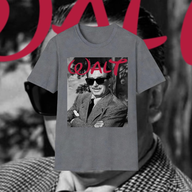 May include: Grey t-shirt with a black and white image of a man in sunglasses and a suit. The word "WALT" is written in red cursive above the image. The background is blurred.