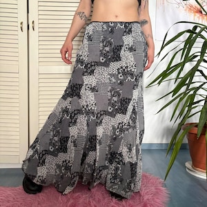 Può includere: Una gonna lunga fino ai piedi caratterizzata da un motivo patchwork bianco e nero con varie stampe floreali e geometriche. La gonna presenta una vita alta con un sottile bordo nero lungo il margine superiore e una silhouette ampia e fluida.