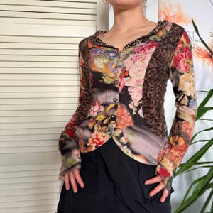 Peut inclure: Haut à manches longues à imprimé floral avec un devant boutonné. Le haut présente un mélange de couleurs, dont le rose, le rouge et le marron, avec un col et des poignets à imprimé léopard. Le vêtement est associé à une jupe noire.