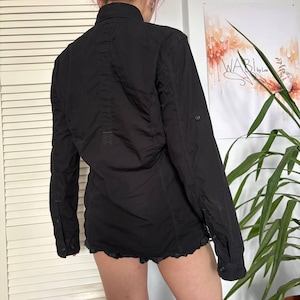 May include: A black long-sleeved button-down shirt featuring a classic collar, a vertical stitched panel down the centre back, and buttoned cuffs. The shirt has a structured fit with visible seams and a button tab on the sleeves for rolling them up.