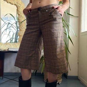 May include: Brown and black plaid culottes featuring a high-waisted design with a single front button closure, two side pockets, and decorative button-down flaps at the waistline. These wide-leg trousers fall to mid-calf length with a structured fit.