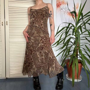 May include: A brown floral print slip dress with spaghetti straps. The dress features a flowing, midi-length skirt and is paired with black boots. The floral pattern includes shades of brown and beige.