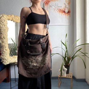 Può includere: Una borsa a tracolla in tela marrone scuro con una grande stampa grafica chiara di ali stilizzate e il testo "Esprit" sul davanti. La borsa include due manici superiori, una lunga tracolla regolabile e dettagli in similpelle marrone scuro.