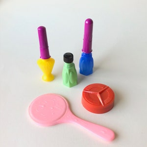 May include: A collection of colorful, vintage plastic toys. Includes a yellow and purple nail polish bottle, a green bottle with a black cap, a blue and purple bottle, a pink hand mirror, and a red container.