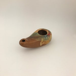 May include: A handmade ceramic oil lamp with a brown base and a colorful top. The lamp features a small spout and a circular opening. The top has a mix of red, blue, and green colors.