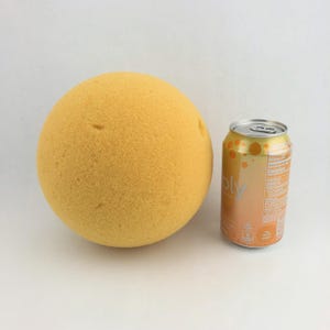 May include: A large, round, yellow sponge ball next to a can of orange-flavored sparkling water. The can has a gradient design with the word "Bubbly" on it.