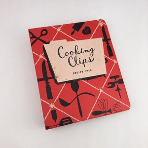 May include: A red recipe file titled "Cooking Clips" with a retro design. The cover features black kitchen utensil illustrations and a white diamond pattern. The recipe file is a vintage item.