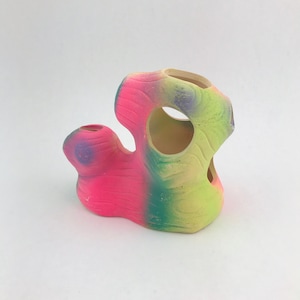 May include: A colorful, abstract ceramic aquarium decoration. The coral-shaped ornament features a gradient of pink, green, and yellow hues. It has multiple openings and a textured surface, suitable for aquatic environments.