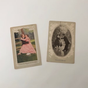 May include: Two vintage postcards. One features a couple embracing with the text "I Love My Wife, but Oh You Kid!". The other shows a couple in a rainy scene with the text "Pleased to meet you."