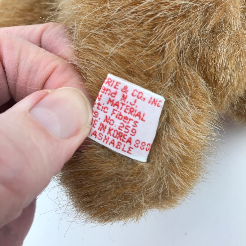 May include: Close-up of a plush toy's fur with a tag. The tag is white with red text, reading "RIE & CO., INC. and N.J. MATERIAL tic Fibers s. No. 259 DE IN KOREA 380 WASHABLE."