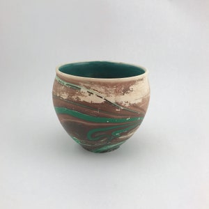 May include: A ceramic bowl with a marbled design. The bowl features a white rim and a teal interior. The exterior has a brown, white, and green swirl pattern. The bowl is round and has a wide opening.