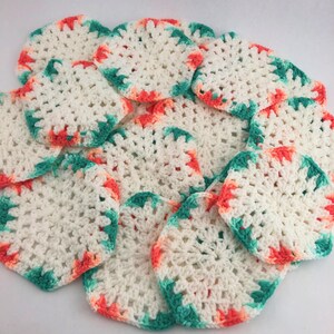 May include: A collection of white, crocheted coasters with a scalloped edge. The edges are accented with alternating coral and teal colors. The coasters are round and appear to be handmade.