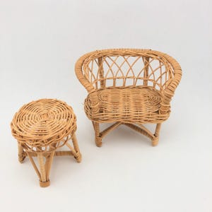 May include: A miniature light brown wicker chair and a matching round wicker stool. The chair features a curved backrest with a crisscross woven pattern and a flat seat. The stool has a circular top and four legs connected by a cross brace.