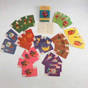 May include: A vintage Crazy Faces card game set. The game includes a box with a cartoon character, playing cards with various whimsical characters, and instruction sheets. The cards are arranged in a circular pattern, showcasing the colorful illustrations.