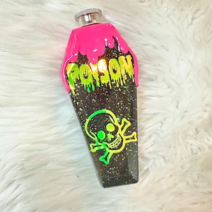 May include: A black flask with a silver cap, shaped like a coffin. The flask has a neon pink top with the word "POISON" in dripping green letters. A neon green skull and crossbones graphic is on the front.