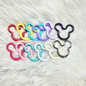 May include: A collection of twelve spring-loaded metal carabiner clips shaped like mouse heads. The clips are arranged in two rows and feature a variety of colors including red, yellow, blue, purple, lavender, black, pink, teal, white, cream, and silver.