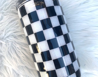 May include: A black and white checkered tumbler with a clear lid. The tumbler is covered in glitter.