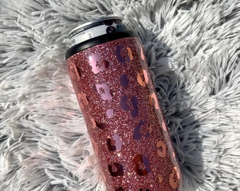 May include: A rose gold glitter tumbler with a leopard print design. The tumbler is made of stainless steel and has a black lid.