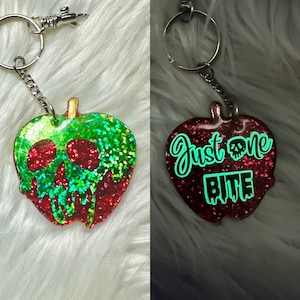 May include: A red and green glitter apple keyring with a skull design. The back of the keyring glows in the dark and says "Just one bite".