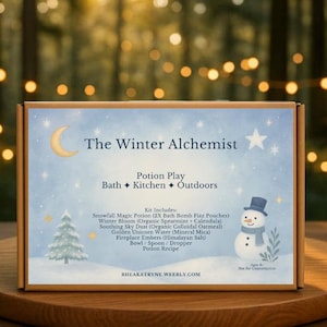 May include: A product box labeled "The Winter Alchemist" with a winter theme. The box features a snowman, a Christmas tree, and the text "Potion Play". The box is on a wooden surface with a blurred background of lights.
